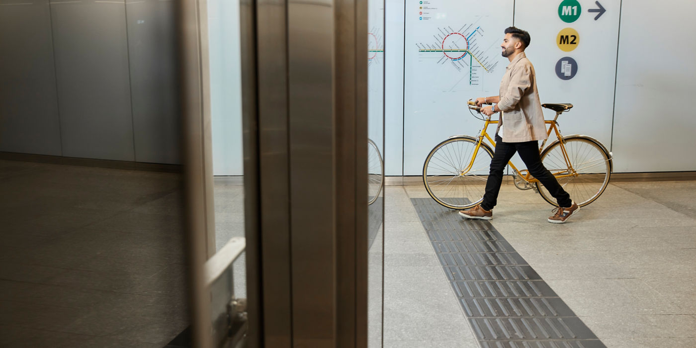 En mann triller sykkelen sin ved en t-banestasjon.